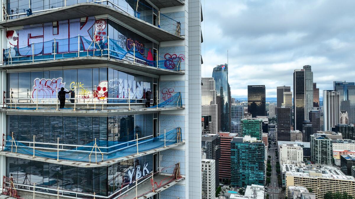 A person in dark clothing is shown near the graffitied glass facade of one of the floors of a skyscraper 